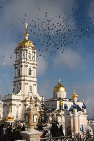 Flock of pigeons flies over the bell tower and Trinity Cathedral of Holy Dormition Pochayiv Lavra, Pochayiv, Ukraineの写真素材