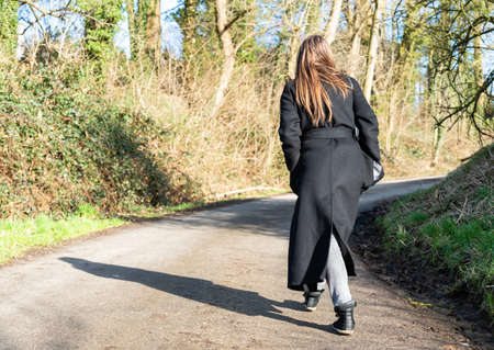 Attractive girl in long black winter coat walking though the muddy paths of the Flemish countryside, Merchtem, Belgiumの写真素材