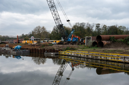 Erembodegem, East Flemish Region, Belgium, 11 04 2022 - Industrial cranes and cargo containers of a harbor reflecting in the River Denderのeditorial素材
