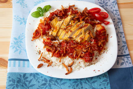 Rice with chicken in tomatoes, fried sausage, sauce on a wooden board and a blue napkin, sprinkled with parmesan cheeseの写真素材