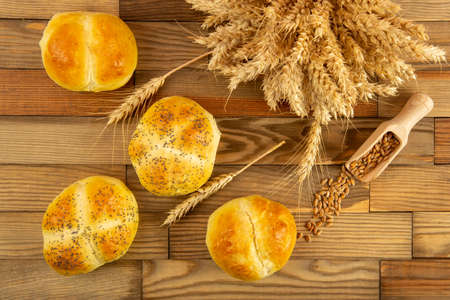 Four buns lying on a wooden table next to the grains and ears of wheat. View from above.の写真素材