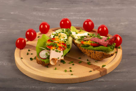 Sandwiches with vegetables, ham, tomatoes, egg on a wooden table and a gray background. Tomatoes in the background.の写真素材
