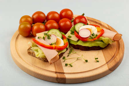 Sandwiches with vegetables, ham, tomatoes, egg on a wooden table and a light background. Tomatoes in the background.の写真素材