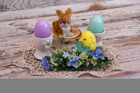Easter rabbit on a stump with Easter egg flowers and candles in the shape of eggs.の写真素材