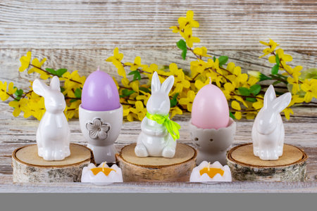 Easter rabbits and Easter egg shaped candles along with a bouquet of flowers on a wooden table.の写真素材