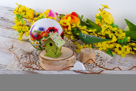 A spring arrangement of flowers with a candle, a wooden bird and a birdhouse.の写真素材
