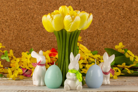 A tulip-shaped candle with Easter eggs, Easter bunnies and a bouquet of flowers on a brown background.の写真素材