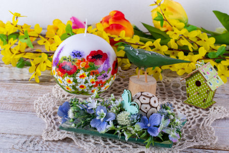 A spring arrangement of flowers with a candle, a wooden bird and a birdhouse.の写真素材