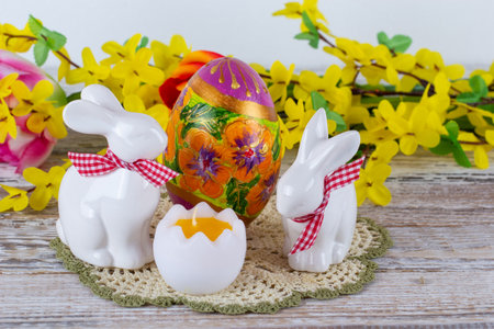 Easter bunnies, Easter eggs and an egg-shaped candle with a bouquet of flowers in the background on a wooden table.の写真素材