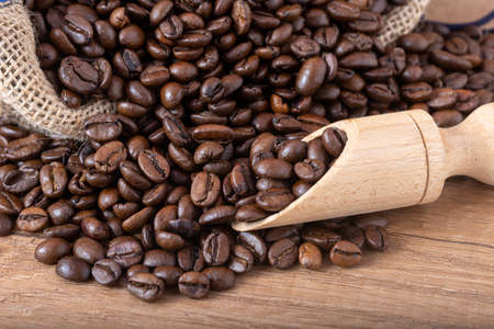 Roasted black coffee beans with a wooden spoon spilling onto the table.の写真素材