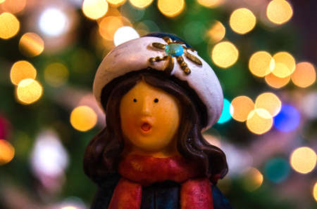 Figure of girl caroler in front of bokah lighted Christmas tree lights.の写真素材