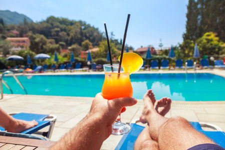 Young Man enjoying whit pineapple cocktail at the swimming pool. Man holding alcohol drink and lying...