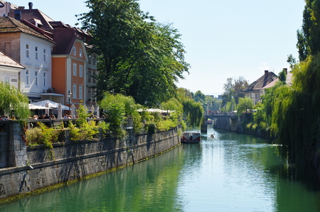 Ljubljana, Slovenia, September 25, 2016, City center, Ljubljanica River, on the river is a tourist ship. Some people are sitting in Their garden coastal pub.のeditorial素材