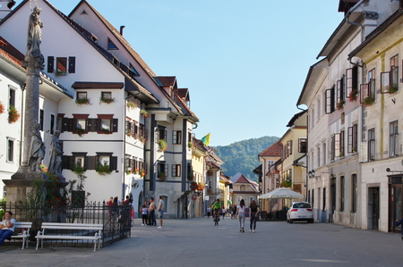 Commune Skofja Loka, Skofja Loka, Slovenia - September 25, 2016, the old town, Mestni trg (City Square). Typical buildings, windows decorated with flowers. Some people are on the street. On the left there is statue of Saint Mary.のeditorial素材