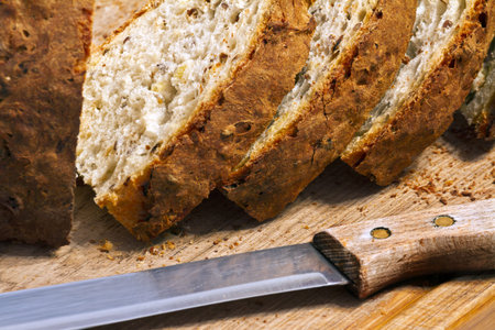 bread crumbs, a knife and a few loaves of fresh bread with a crispy crust on a wooden board