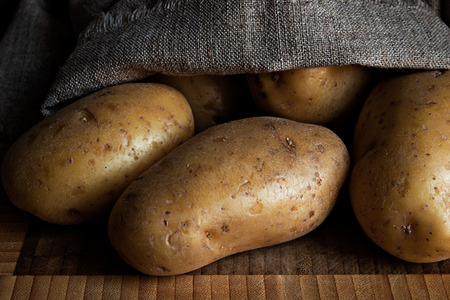potatoes, spill out canvas bag on a wooden boardの写真素材