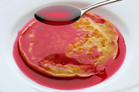 spoon with cherry syrup over pancakes on a white plateの写真素材