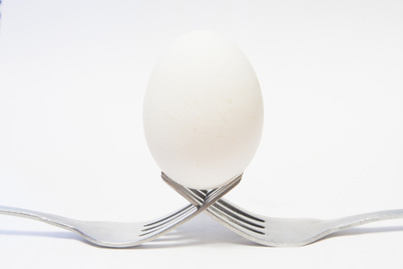Egg balanced on two metal forks, white backgroundの写真素材