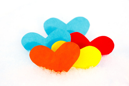 Five paper colored heart shapes in snowの写真素材