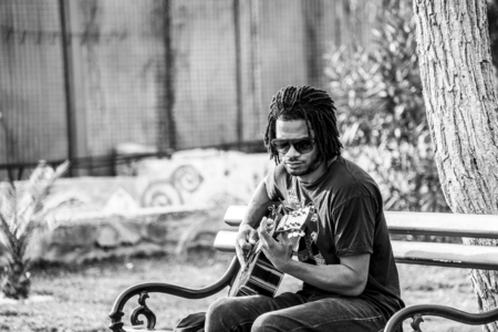 Budva, Montenegro, February 05, 2019: Black African guy with dreadlocks is sitting on a bench on the embankment, playing guitar and singing to make moneyのeditorial素材