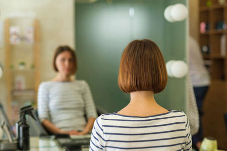 Forty-year-old woman had her hair cut and styled in a beauty salon. She smiles at the camera, sitting with her back to the mirrorの写真素材