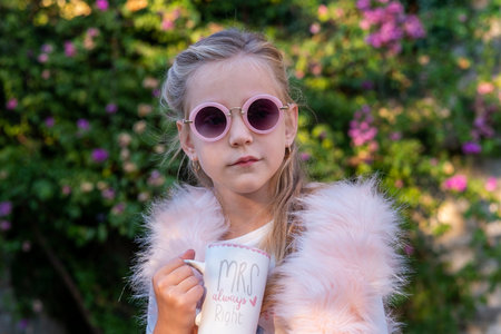 Seven-year-old girl, blonde with long hair, wearing round sunglasses and a pink fur vest, on a walk...