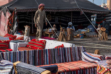 Hurghada, Egypt, November 03, 2021: An Arabic-style cafe with low armchairs, sofas and tables for drinks, guests drinking tea and coffee in the shade inside the tent, an African man brewing coffee on coals, an Arab, a cafe employee serves new visitors.のeditorial素材