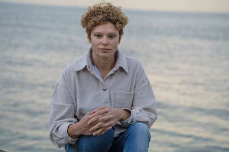 Portrait of a smiling european girl with short brown curly hair wearing beige corduroy shirt against...