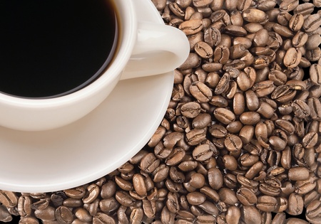 Freshly brewed coffee in white cup over dark roasted coffee beansの写真素材