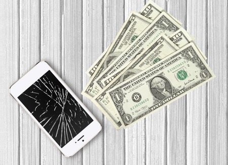 Modern broken mobile phone and dollars on white wooden backgroundの写真素材