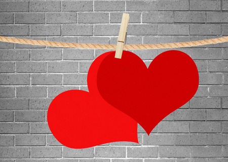 two red hearts hang on clothespin over grey brick wallの写真素材