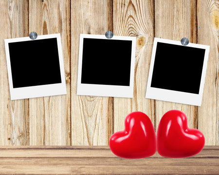 Blank old photos on clips and red hearts on wooden background
