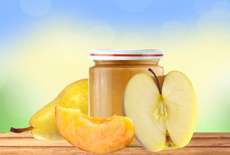 Jar of baby puree, fresh apple, peach and pear on wooden table over bright nature backgroundの写真素材