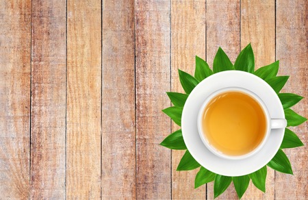 White Tea Cup on Green Leaves on Brown Old Wood Plank Texture Backgroundの写真素材