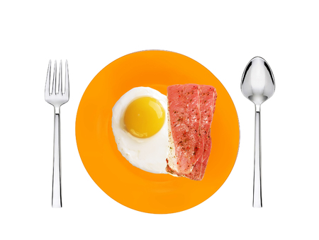 Scrambled eggs and roasted bacon with spices on orange plate with spoon and forkの写真素材
