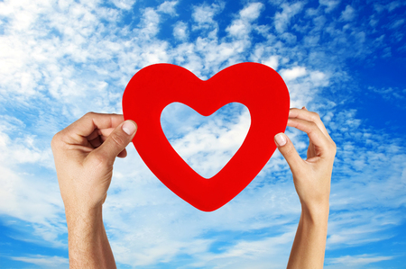 hands holding heart shape with blue sky backgroundの写真素材
