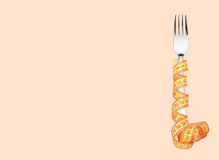Measuring tape wrapped around fork lying on color surface. Diet conceptの写真素材