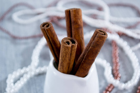 Cinnamon sticks in a white glass, beads on a blue background