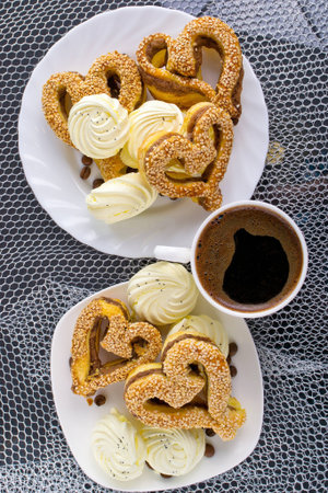 heart-shaped pastry with sesame seeds, marshmallow and a cup of coffee on a silver background