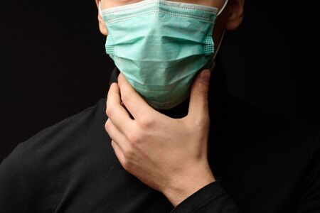 Young woman wearing medical mask protecting from virus. Serious female with sad eyes touching protection mask from dangerous coronavirus epidemic and looking at camera on black backgroundの写真素材