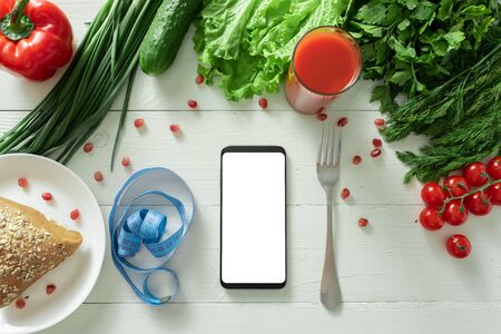 The smartphone lies on a table with diet vegetables. Place for your text.の写真素材