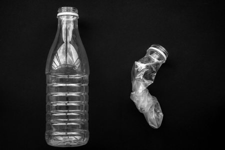 A squeezed and whole plastic bottle on a black background. The concept of saving the environment.