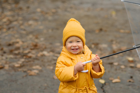A little girl walks with an umbrella in yellow rubber boots and a waterproof raincoat. Autumn Walk.