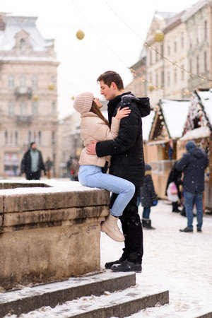 Having fun together at a christmas fairy with snowfall. Young cheerful couple is having a walk, enjoying, dressed warm, looking at each other and laugh, snowflakes all around.の写真素材