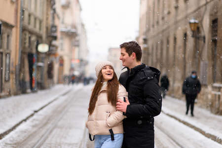 Having fun together at a christmas fairy with snowfall. Young cheerful couple is having a walk, enjoying, dressed warm, looking at each other and laugh, snowflakes all around.の写真素材