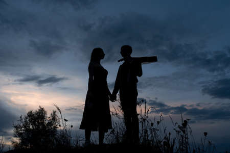 Silhouette of a couple in love on a date. The man holds the girl's hand. The guy in crabs has a guitar. Filmed at sunset.の写真素材