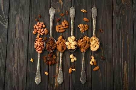 Hazelnut, cashews, raisins, almonds, peanuts, walnuts in silver spoons on a rustic background