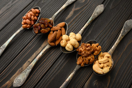 Hazelnut, cashews, raisins, almonds, peanuts, walnuts in silver spoons on a rustic background