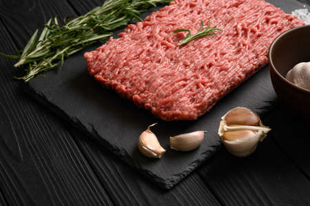 Fresh raw meat or ground chicken meat on a wooden cutting board with thyme, spices and garlic. Black wooden background. top view. copyspace.の写真素材