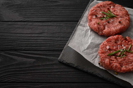 Raw beef burger patties on butcher's wooden board, rosemary and pepper. Black background. view from above.の写真素材
